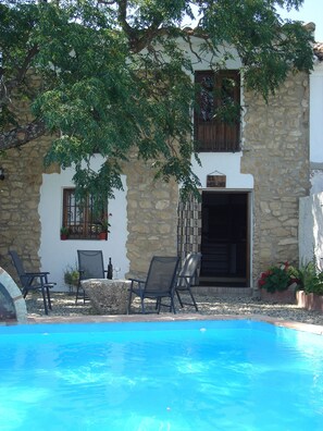 A stone building with a pool, outdoor seating, and potted plants. - Cortijo Molino Los Justos (Algarinejo)