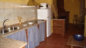 A kitchen with a tiled backsplash, a white refrigerator, a brick oven, and a blue bowl on the counter. - Cortijo Molino Los Justos (Algarinejo)