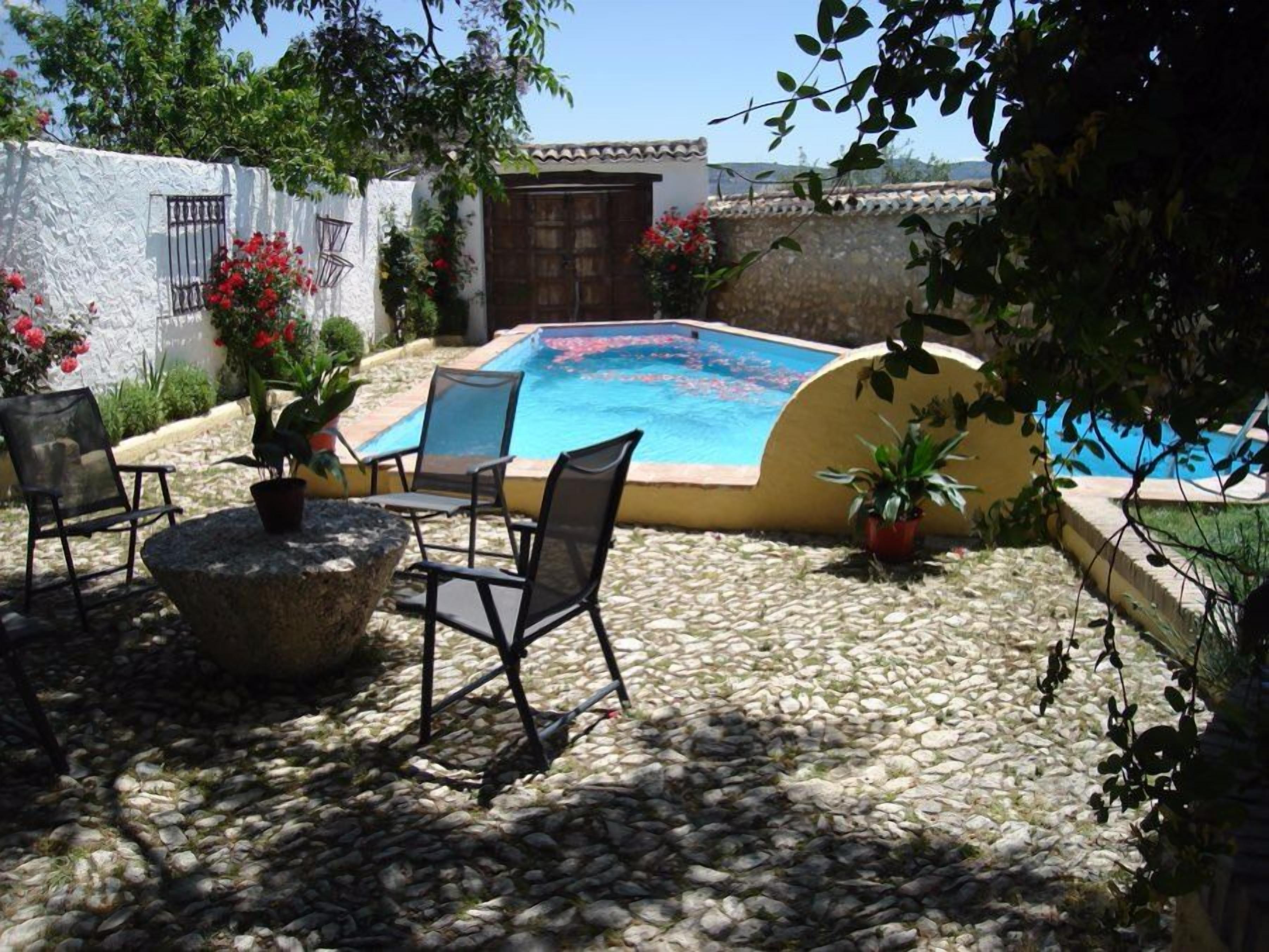 Una zona de piscina con suelo de piedra, algunas sillas y plantas en macetas.