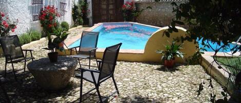 Una zona de piscina con suelo de piedra, algunas sillas y plantas en macetas.
