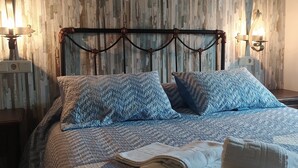 A bed with a patterned quilt and pillows, a headboard with a decorative design, and two wall-mounted lamps. - Cortijo Molino Los Justos (Algarinejo)
