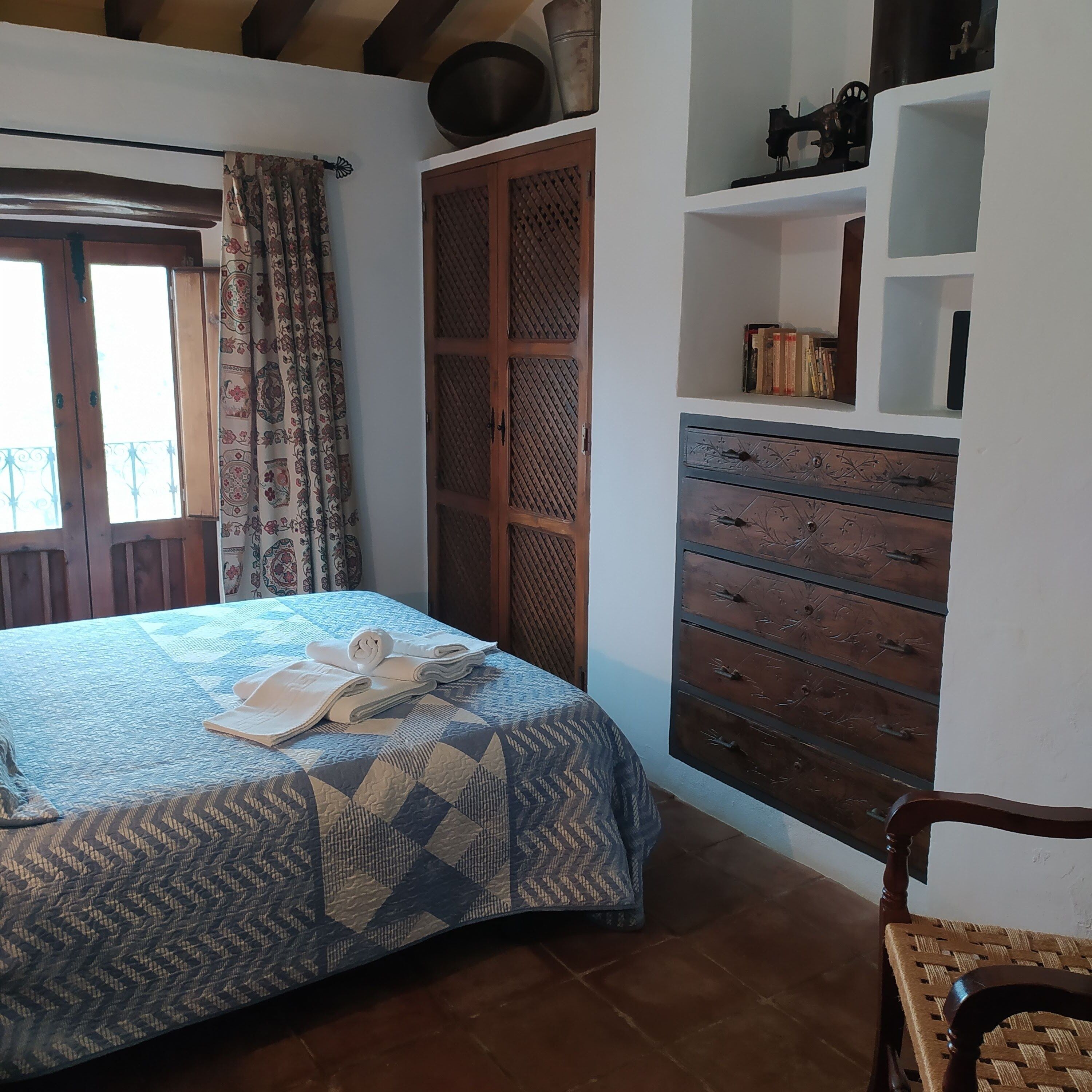 Une chambre à coucher avec un lit, une armoire en bois, une étagère remplie de livres et une fenêtre avec des rideaux.