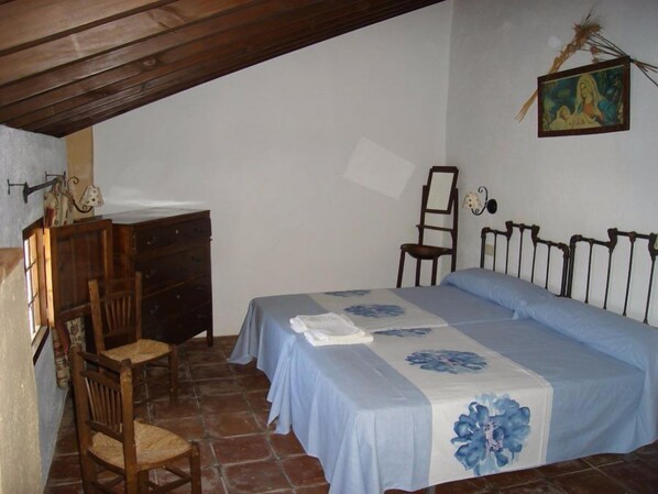 A bedroom with a bed, a wooden chair, a desk, and a painting on the wall. - Cortijo Molino Los Justos (Algarinejo)