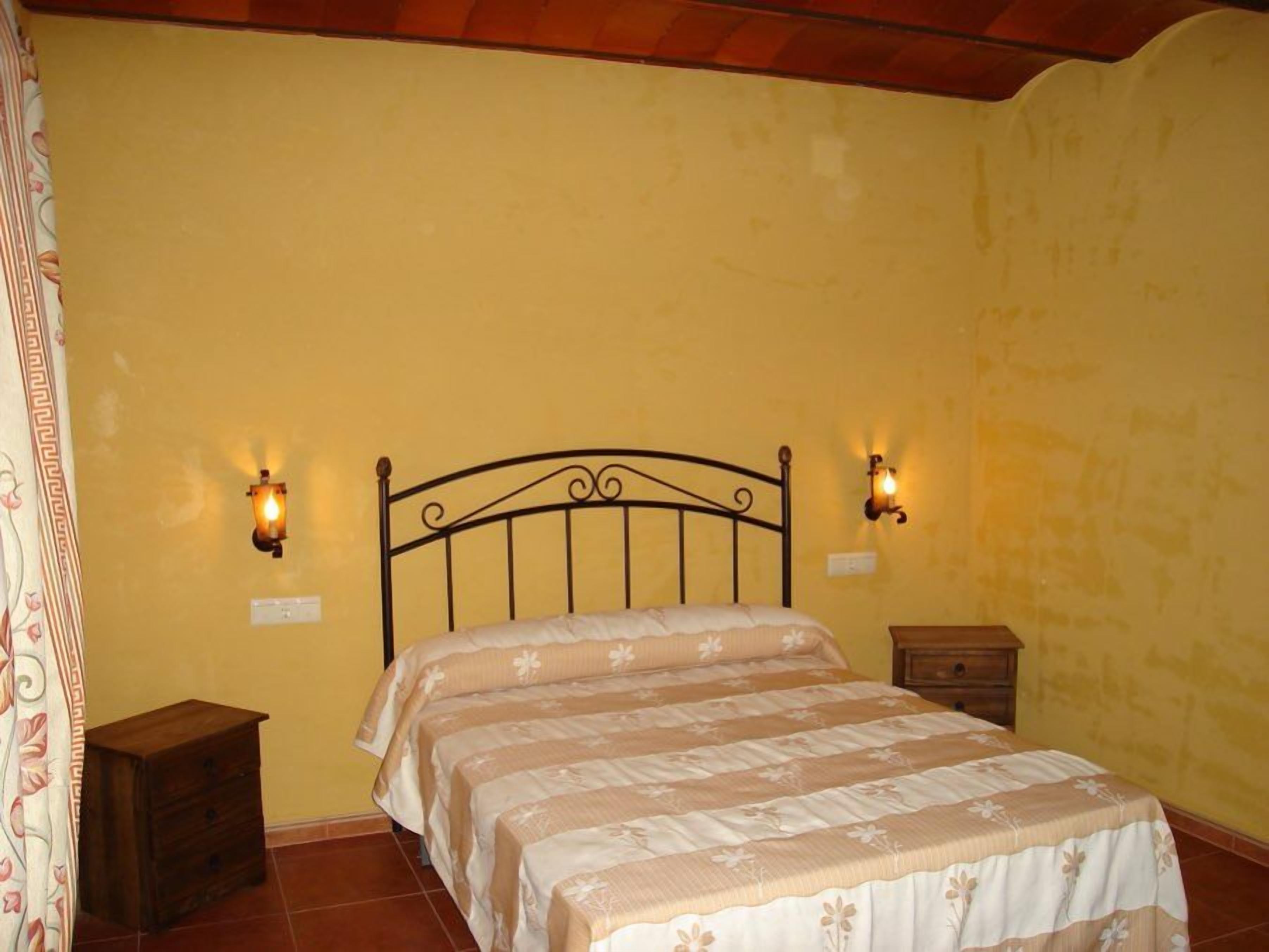 Un dormitorio con cama, dos mesitas de noche y luces fijadas a la pared.