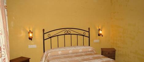 Un dormitorio con cama, dos mesitas de noche y luces fijadas a la pared.