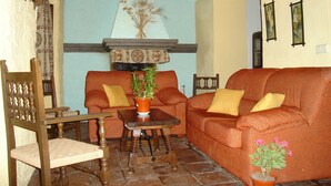 A cozy living room with a wooden chair, a sofa, a small table, and a potted plant. - Cortijo Molino Los Justos (Algarinejo)