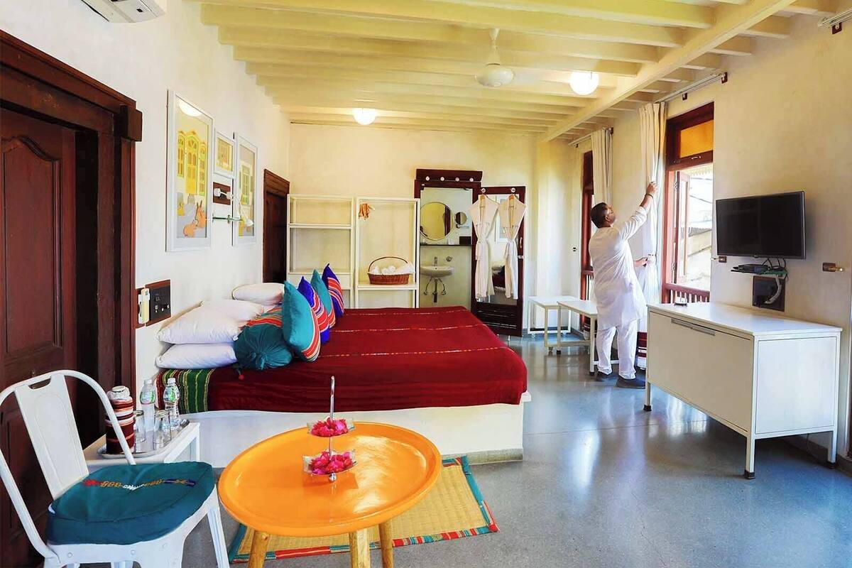 Ein Hotelzimmer mit Bett, Schreibtisch, Fernseher und einem durchgegangenen Tür erkennbaren Badezimmer.