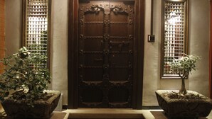 A wooden double door with intricate carvings, flanked by two potted plants. - Mangaldas Ni Haveli II by The House of MG (Ahmedabad)