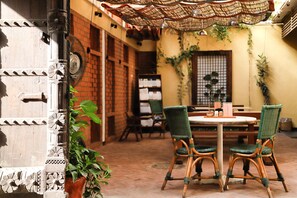 An outdoor patio with a round table and four wicker chairs, surrounded by potted plants and a brick wall. - Mangaldas Ni Haveli II by The House of MG (Ahmedabad)