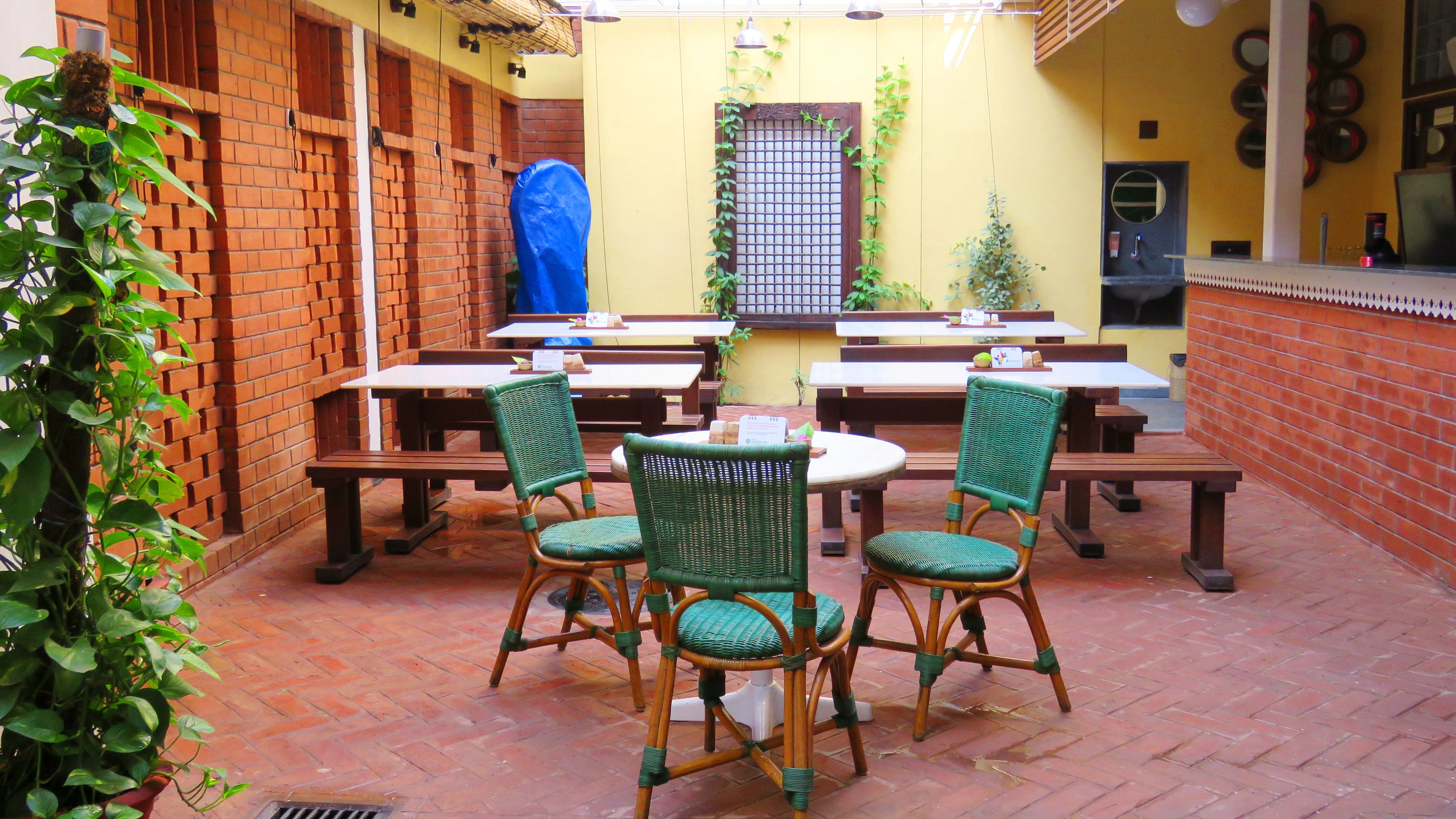 An outdoor dining area with brick walls, green wicker chairs, and wooden tables.