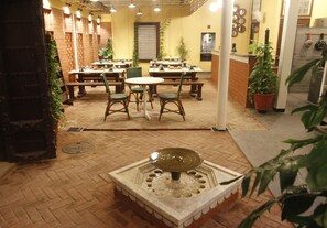 A restaurant with brick walls, wooden tables, and chairs, featuring a central decorative fountain.
