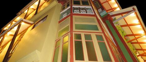 Un edificio de varios pisos con un estilo arquitectónico distintivo, que presenta un balcón con barandillas ornamentadas y una serie de ventanas con marcos decorativos.