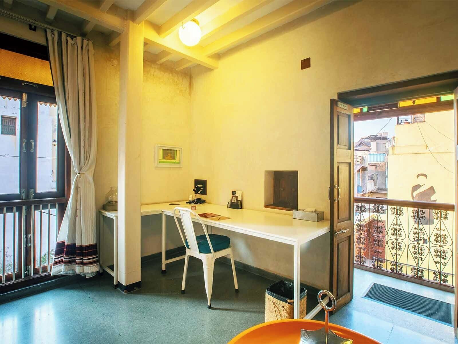 Ein kleiner, kompakter Raum mit Schreibtisch, Stuhl und einem Fenster mit Vorhängen.