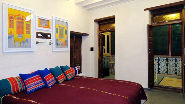 A room with a bed, colorful pillows, and three framed artworks on the wall.