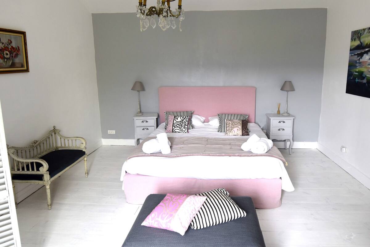 Une chambre à coucher avec un lit, des tables de chevet, une chaise et un lustre.