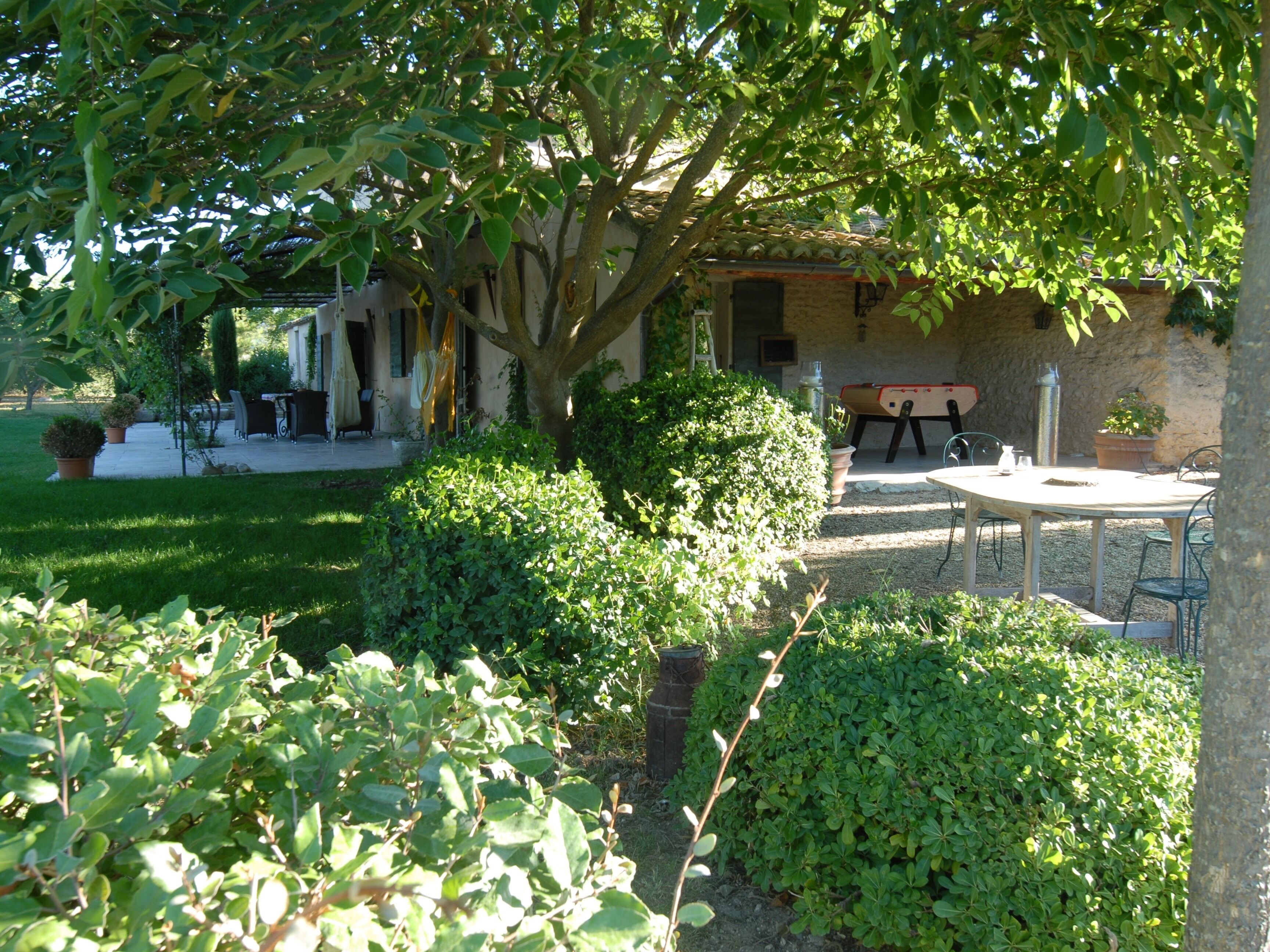 A patio area with a table and chairs, surrounded by lush greenery and a building with a tiled roof.