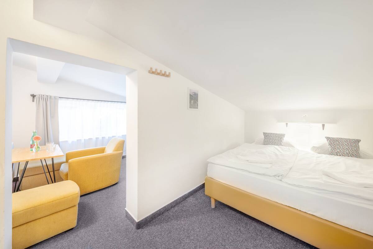 A hotel room with a bed, a small table with chairs, and a window with curtains.