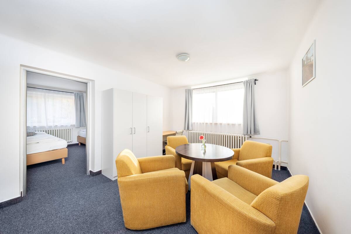 A hotel room with a bed, a round table with chairs, and a view of the outdoors.