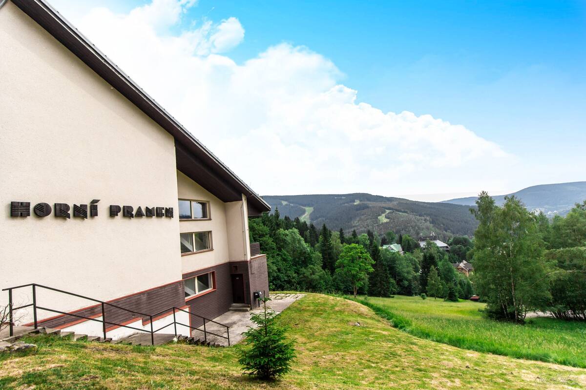 A building named "Horní Pranice" with a staircase leading to the entrance, surrounded by greenery and hills in the background.