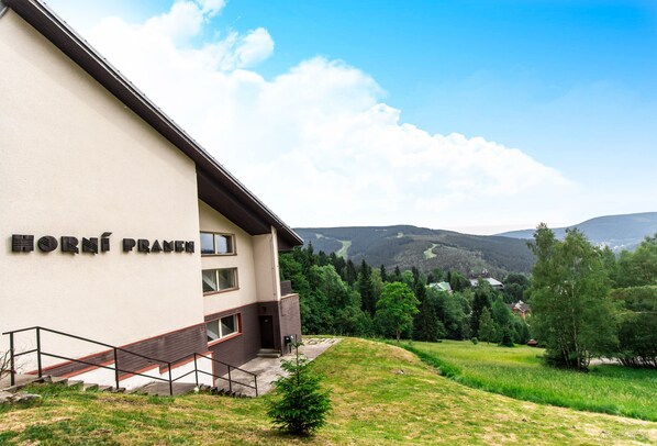 A building named "Horní Pranice" with a staircase leading to the entrance, surrounded by greenery and hills in the background.