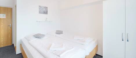 A bedroom with a bed, two pillows, a bedside table, a wardrobe, and a small shelf with a picture.