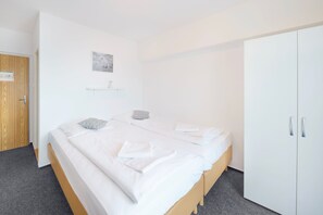 A bedroom with a bed, two pillows, a bedside table, a wardrobe, and a small shelf with a picture.