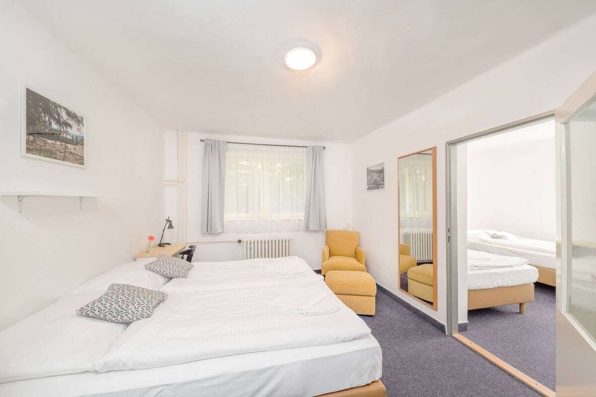 A hotel room with two beds, a window with curtains, a chair, and a mirror.