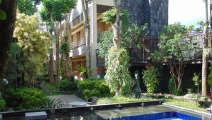 A pool area with a blue tiled floor, surrounded by greenery and trees. - Savita Garden Inn (Ngaglik)