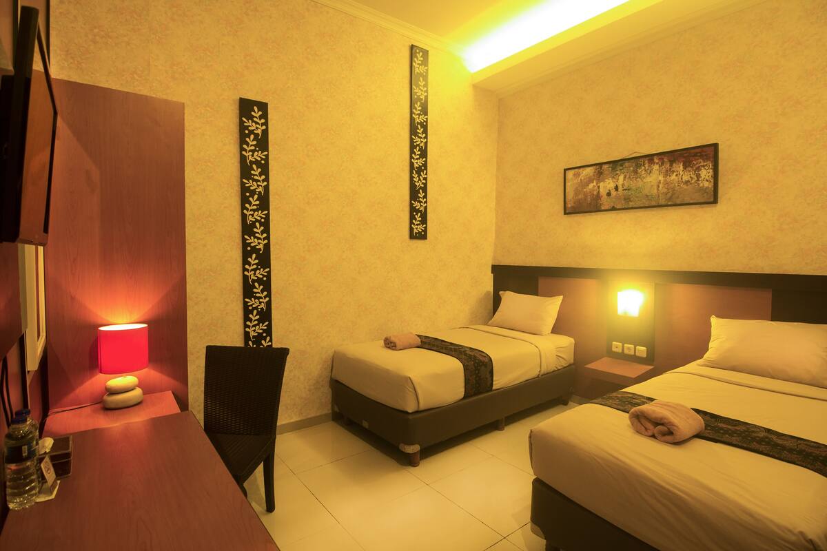 A hotel room with two beds, a desk with a lamp, and a wall-mounted artwork.