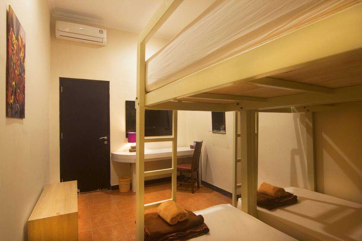 A dormitory room with bunk beds, a desk, a chair, a sink, and an air conditioning unit.