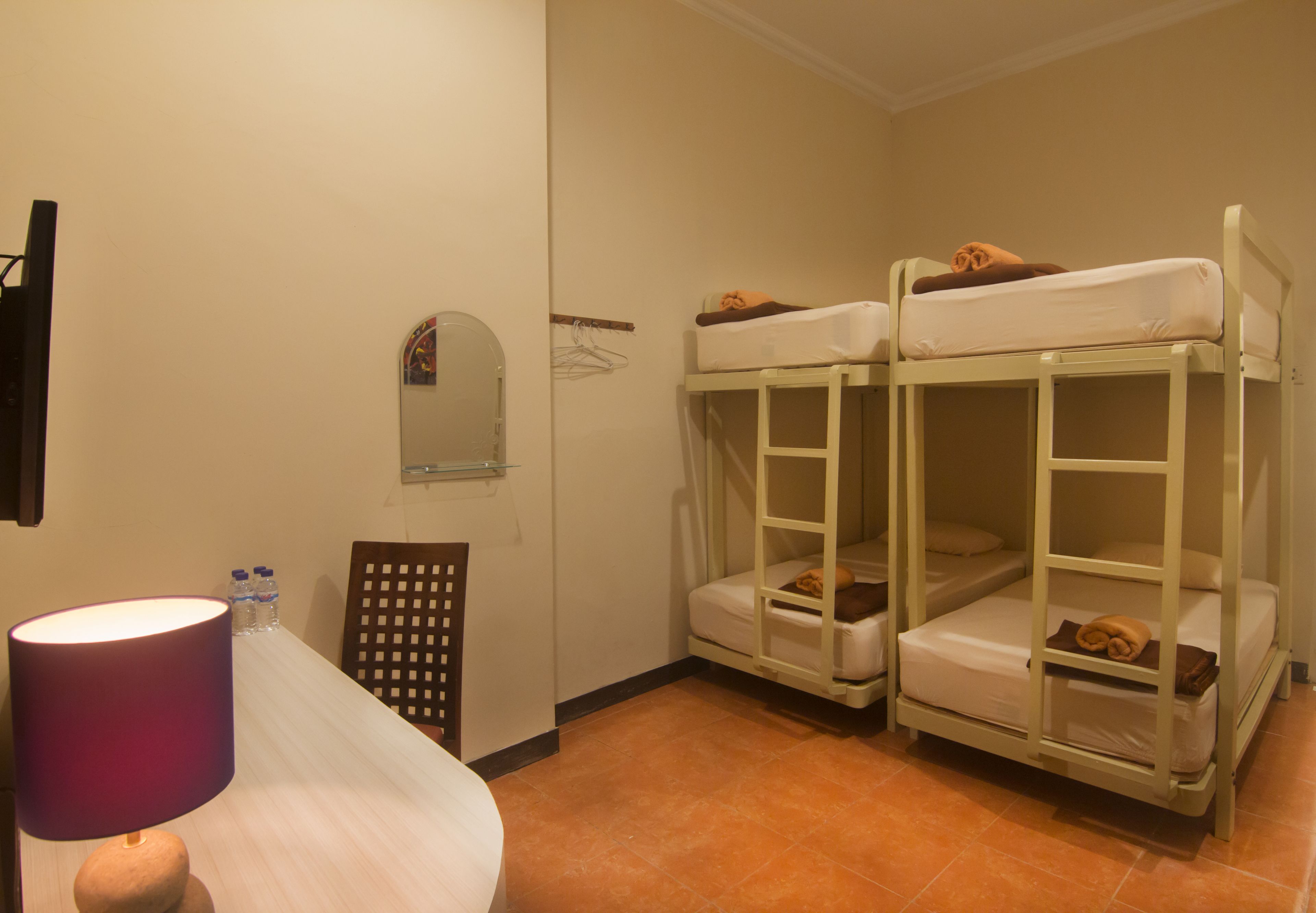 A room with bunk beds, a table with a lamp, and a small mirror on the wall.