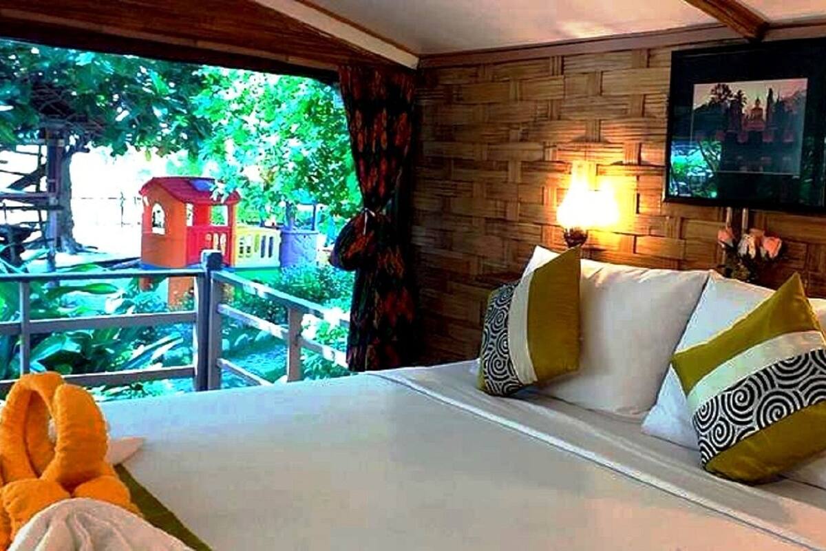Une chambre d’hôtel avec un lit, deux lampes de chevet, une fenêtre donnant sur un terrain de jeux et un mur en bois.