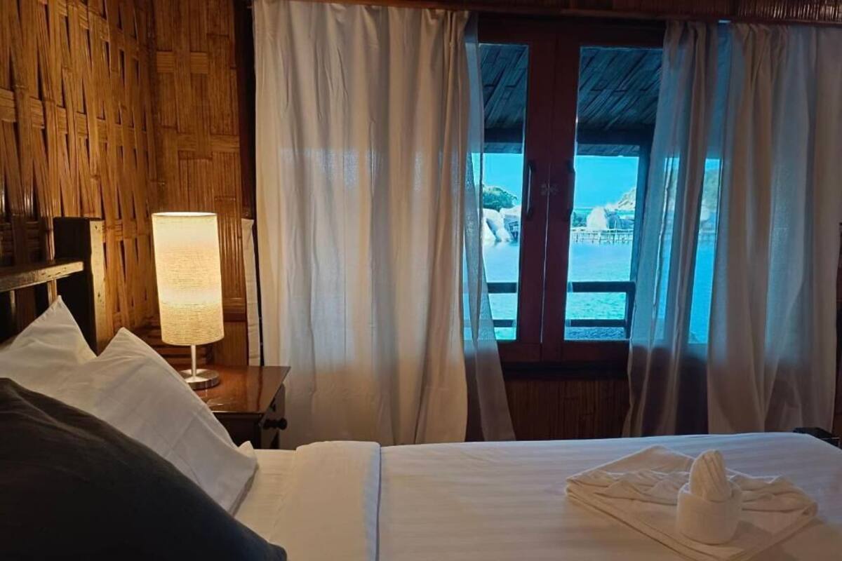 Une chambre d’hôtel avec un lit, une table de chevet avec une lampe et une vue sur la mer grâce à de grandes fenêtres.