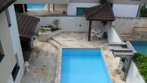 A swimming pool with tiled flooring, a pergola, and a small table with chairs. - Bougainville 1 Frente ao Mar de Peruíbe (Peruíbe)