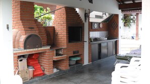 An outdoor kitchen area with a brick oven, a sink, and a countertop. - Bougainville 1 Frente ao Mar de Peruíbe (Peruíbe)