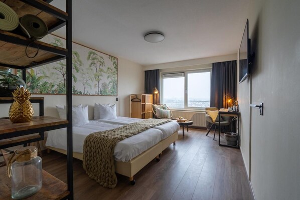 A hotel room with a large bed, a desk with a chair, a television, and a window with a view.