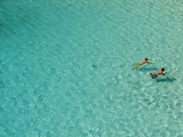 Una piscina azul cristalina con dos personas nadando.