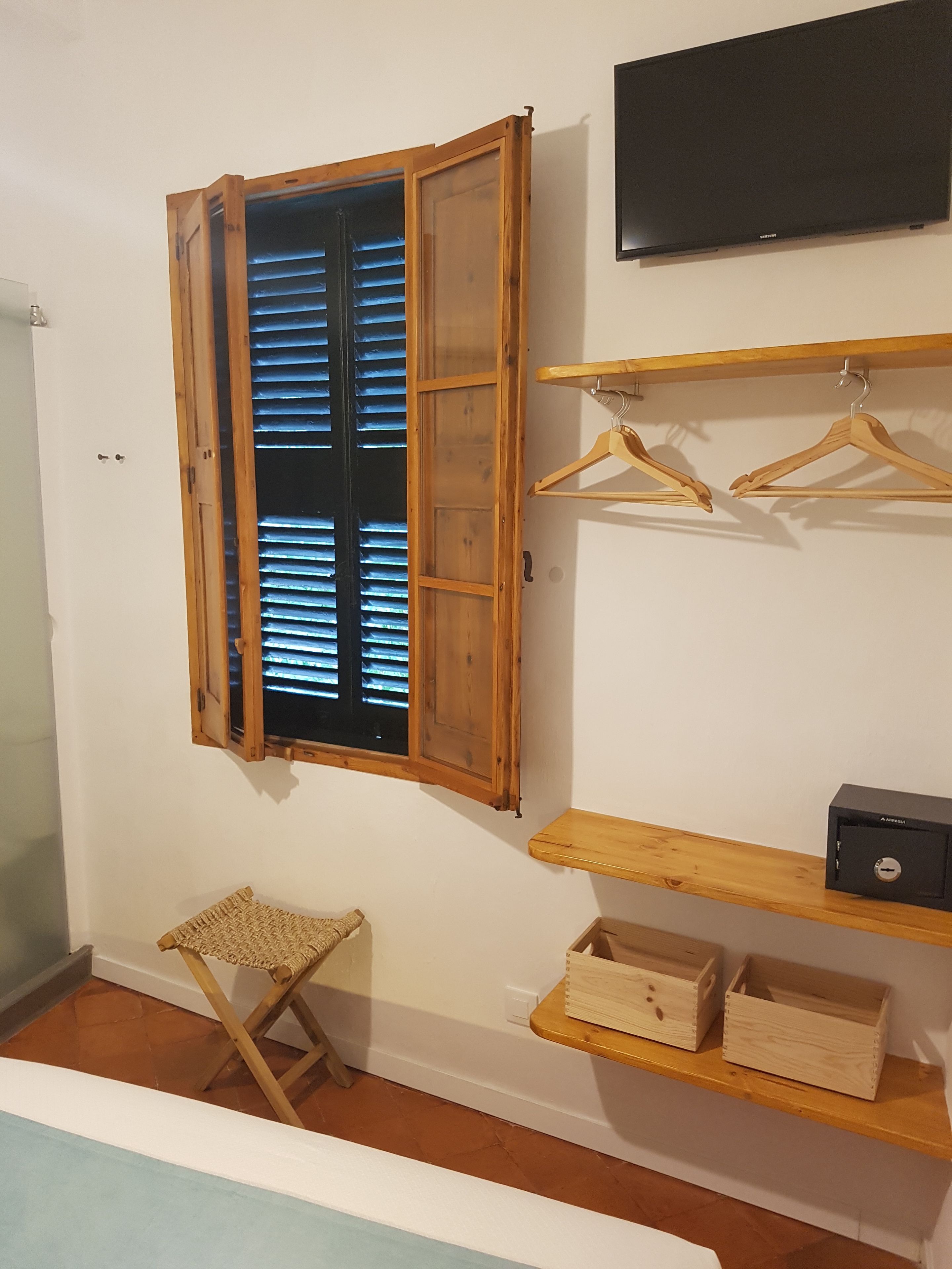 A room with a wooden window, a TV mounted on the wall, wooden shelves, and a small seating area.