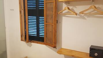 A room with a wooden window, a TV mounted on the wall, wooden shelves, and a small seating area.
