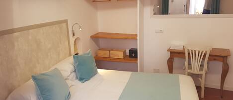 Un dormitorio con cama, escritorio, silla, espejo y estante con ropa colgada.