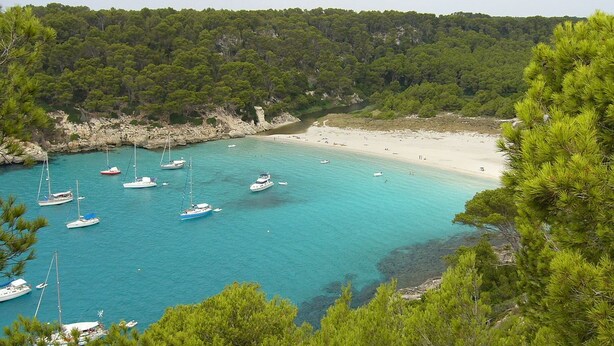 A coastal bay with clear turquoise waters, a sandy beach, and several sailboats anchored near the shore. - My Rooms Ciutadella - Adults Only by My Rooms Hotels (Ciutadella de Menorca)