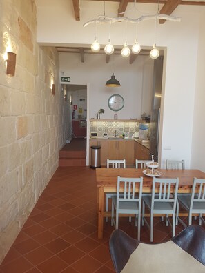 A dining area with a wooden table and chairs, a hanging light fixture, and a kitchen in the background. - My Rooms Ciutadella - Adults Only by My Rooms Hotels (Ciutadella de Menorca)