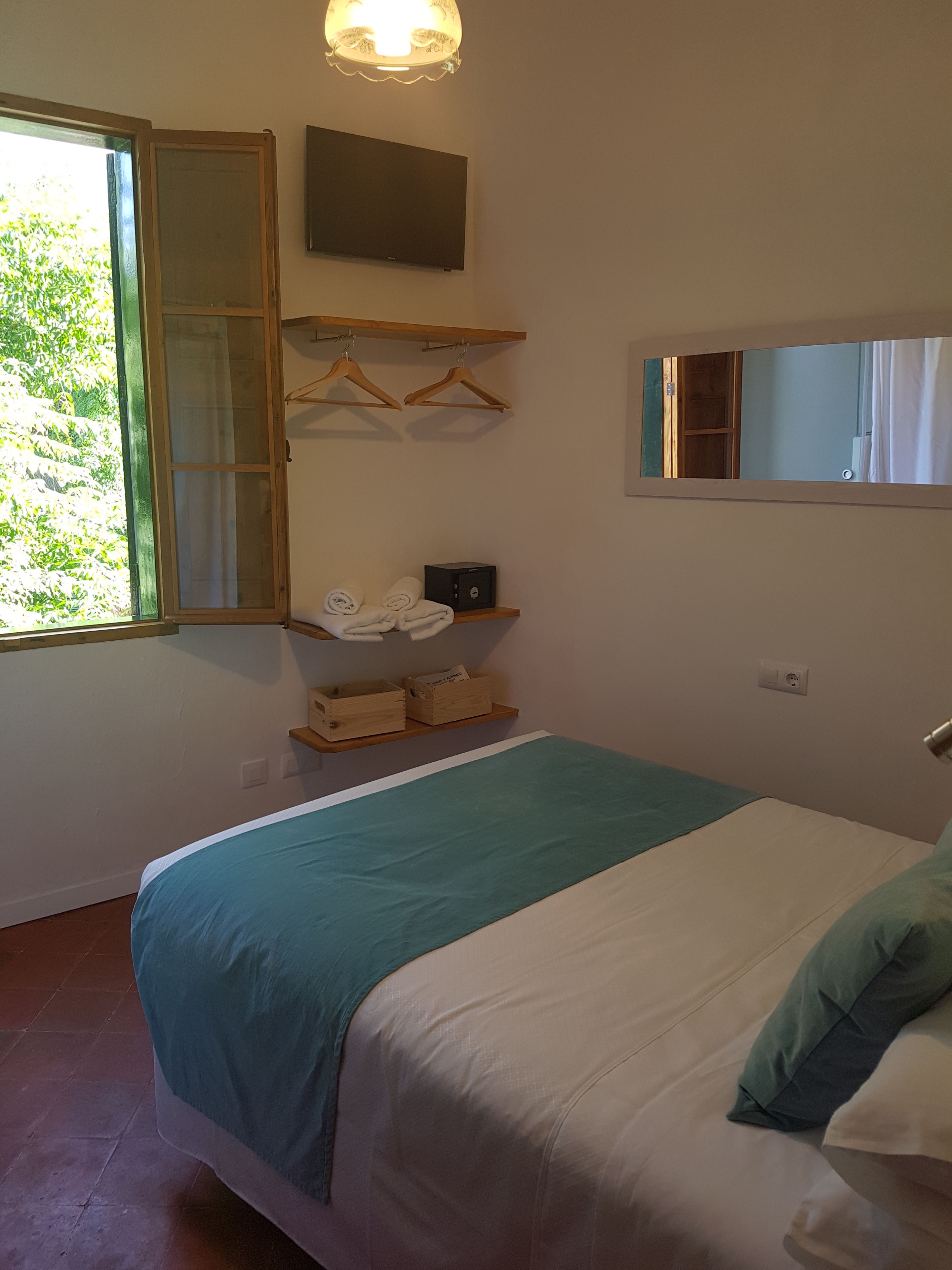 Un dormitorio con una cama, una ventana, un espejo y una estantería con objetos.
