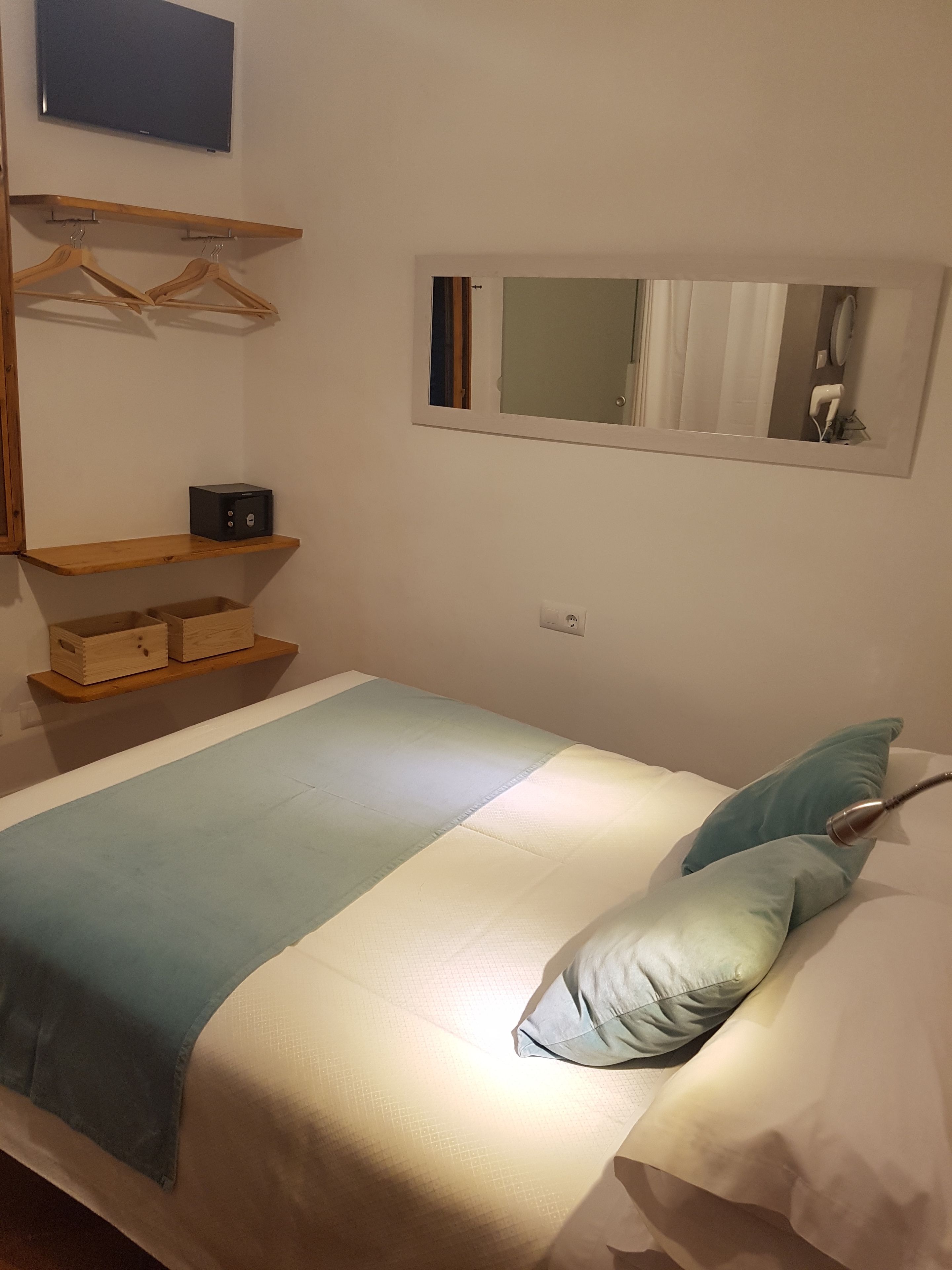 Una camera da letto ordinata con un letto, un comodino, uno specchio e un televisore montato a parete.