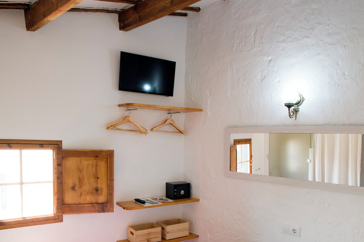 A bedroom with a bed, wooden beams, a television, a mirror, and a window.