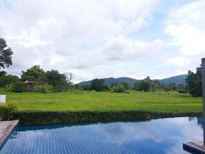 A pool with a tiled edge, surrounded by lush greenery and a distant mountain range. - Mountain View Pool Villa Nakhonnayok (Ban Na)