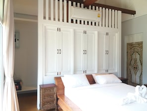 A bedroom with a large bed, white wardrobes, a wooden nightstand, and a decorative mirror. - Mountain View Pool Villa Nakhonnayok (Ban Na)