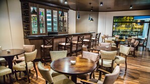 A restaurant with round tables and chairs, a bar area with shelves of bottles, and a view through large windows. - Gaboardi Park Hotel (Curitibanos)
