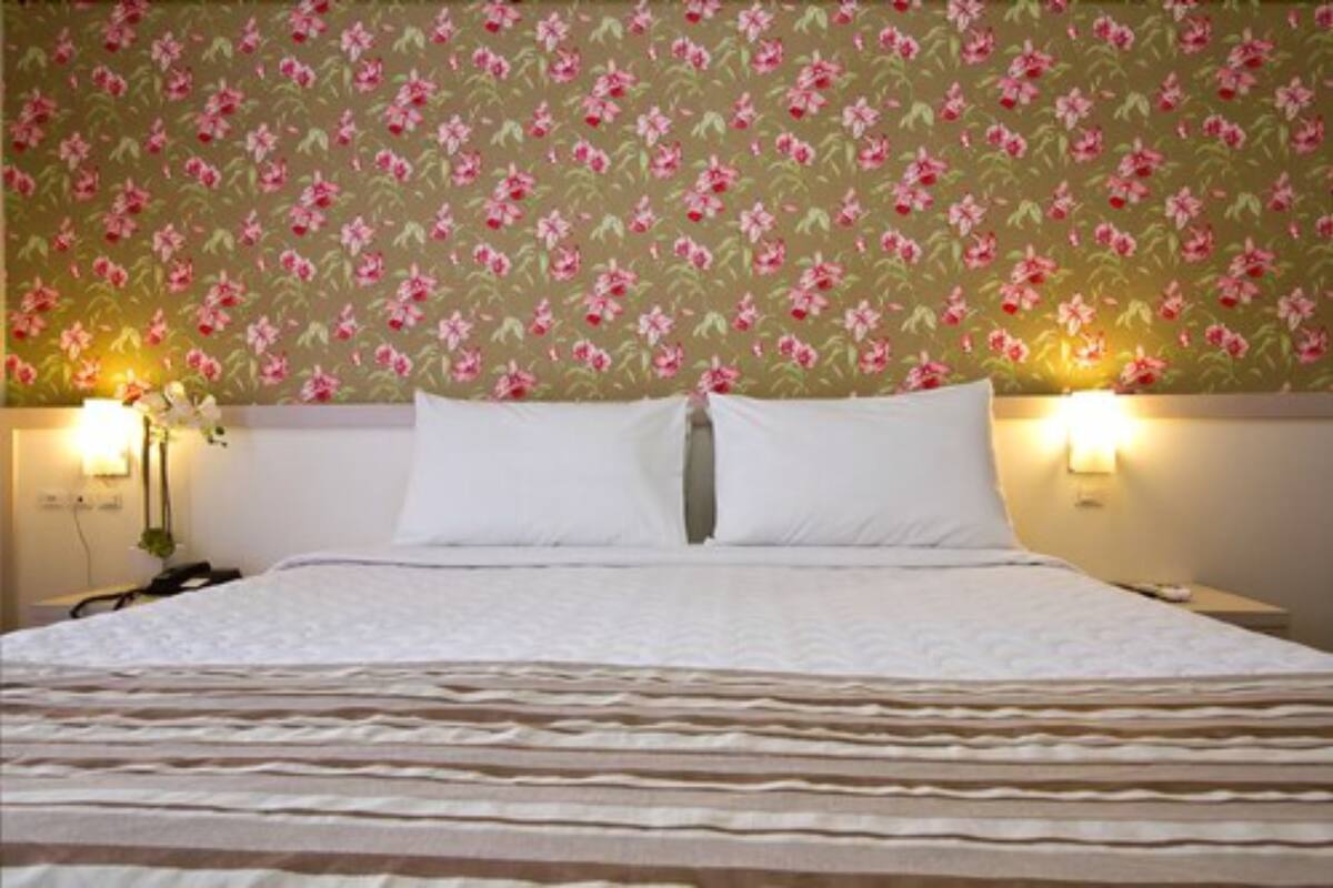 A hotel room with a bed, floral wallpaper, and bedside lamps.
