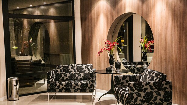 A modern interior with a sofa and armchair, a round table, and a mirror reflecting the room. - Gaboardi Park Hotel (Curitibanos)